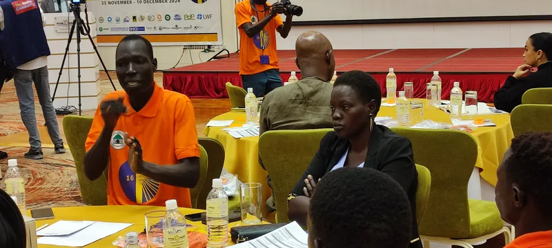 A participant speaks during a group discussion while the event is photographed